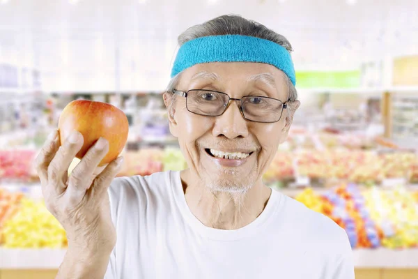 Velho com maçã orgânica no supermercado — Fotografia de Stock