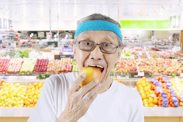Velho comendo uma maçã no supermercado — Fotografia de Stock