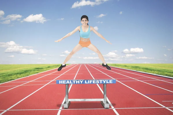 Sporty woman jumping above a hurdle — Stock Photo, Image