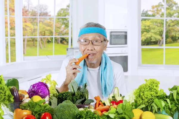 Vieil homme mangeant des carottes dans la cuisine — Photo
