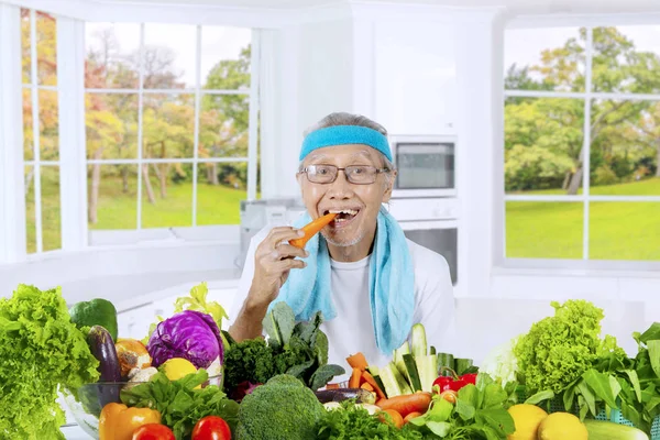 Oude man bijten wortel in de keuken — Stockfoto