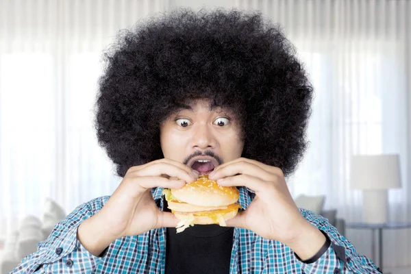 Афро-человек ест большой чизбургер дома — стоковое фото