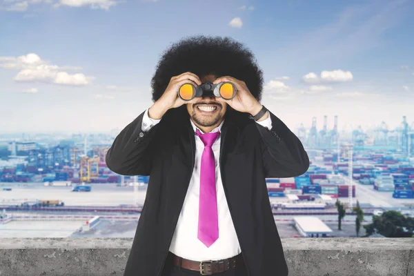 Afro-Geschäftsmann mit Fernglas am Industriehafen — Stockfoto