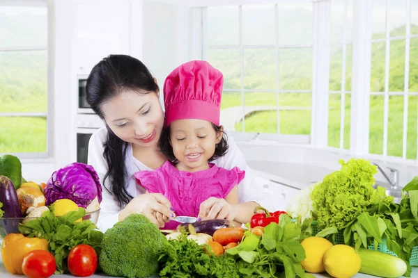Criança feminina e mãe cortar legumes — Fotografia de Stock