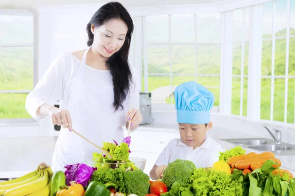 Junge schneidet Gemüse und Mutter rührt Salat an — Stockfoto