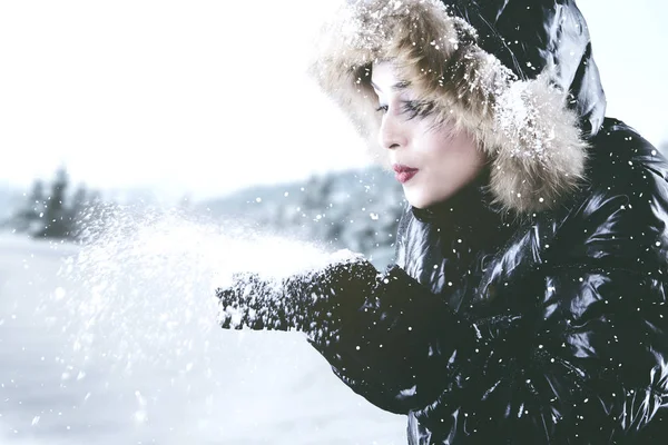 Mooie vrouw waait sneeuw uit handen — Stockfoto