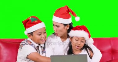 Aile ile Noel Baba şapkası kanepede dizüstü bilgisayar kullanarak