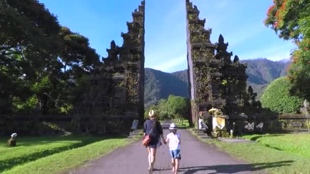 Мать и дочь входят в традиционные балийские ворота — стоковое видео