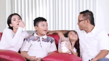 Mutlu aile evde oturma odasında kanepede oturan ve yeme snack iken birlikte televizyon izlerken