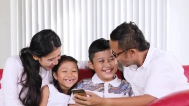 Mutlu aile bir smartphone birlikte sohbet ve evde oturma odasında kanepede oturan süre kullanma.