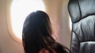 Uçak pencereden dışarı bakarak ve tatil için bir uçuş sırasında kameraya konuşurken şirin dişsiz küçük bir kızın video görüntüleri