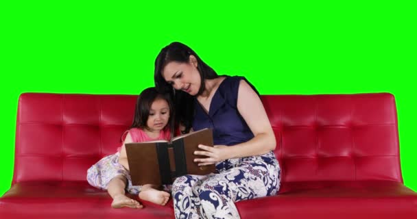 若い母親と娘の赤いソファに座って本を読んでグリーン スクリーンの背景を持つ 解像度で撮影 — ストック動画
