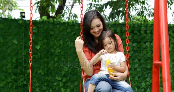 快乐的小女孩和她的母亲吹肥皂泡沫 而坐在公园的秋千 拍摄4K — 图库视频影像