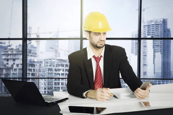 Arquiteto italiano trabalhando com planta e telefone celular — Fotografia de Stock