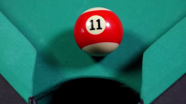 Gros plan d'une boule de billard avec le numéro 11, tombant dans le trou de la table de billard 