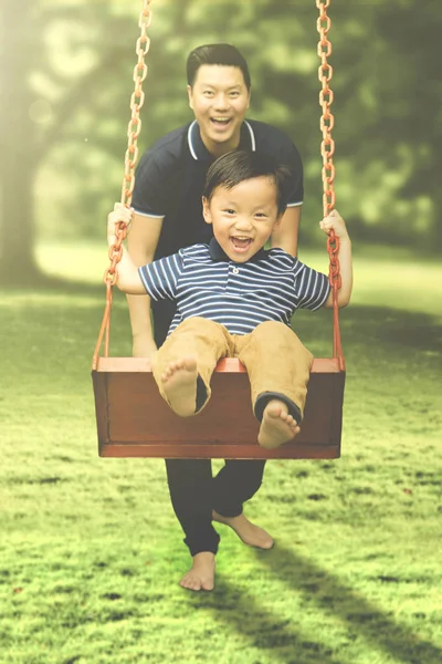 Pai feliz e seu filho brincando com swing — Fotografia de Stock