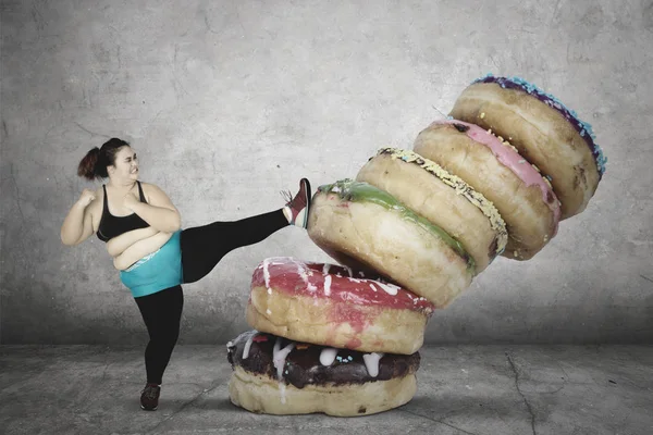 Mulher gorda chutando uma pilha de donuts — Fotografia de Stock