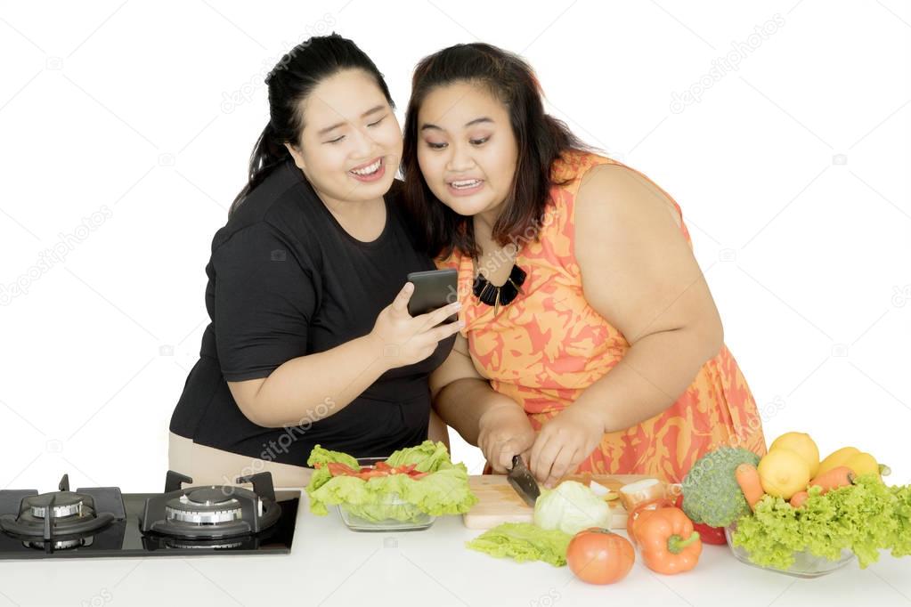 Two obese women cooking together with a smartphone