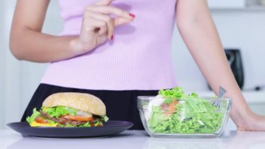 Diyet kavramı. Salata bir kase alın seçme ve bir tabak Burger reddederek bilinmeyen kadın elinde kapatın. 4 k çözünürlükte vurdu