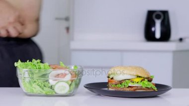 Diyet kavramı. Bilinmeyen kilolu adam salata bir kase hamburger almaya karar vermeden. 4 k çözünürlükte vurdu