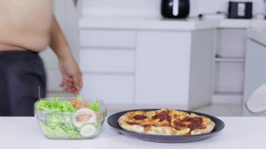 Diyet kavramı. Tanınmayan kilolu adam biberli pizza daha taze salata bir kase almaya karar verir. 4 k çözünürlükte vurdu