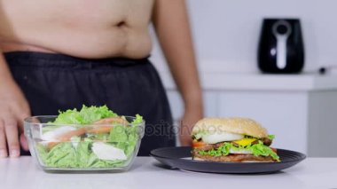 Diyet kavramı. Anonim kilolu adam bir kase salata hamburger daha getirmek seçme. 4 k çözünürlükte vurdu