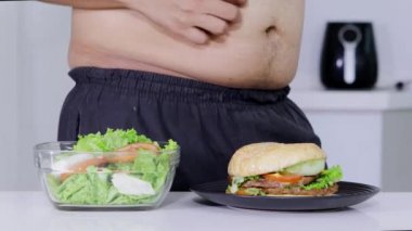 Diyet kavramı. Anonim kilolu adam bir burger veya abur cubur daha salata bir kase seçme jest eller. 4 k çözünürlükte vurdu