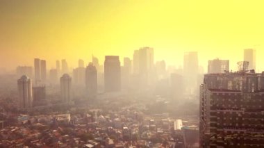 Jakarta - Endonezya. 26 Aralık 2017: Kuş görünümü değil, 4 k çözünürlükte çekim soldan uçan bir dron gün batımından, turuncu gökyüzü ile sis içinde gökdelenler