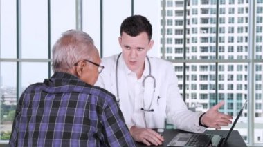 Bir dizüstü bilgisayar ve bir şişe hap ya da onun yaşlı erkek hasta doktor ofisinde uyuşturucu tıbbi sonucu gösterilen erkek beyaz doktor