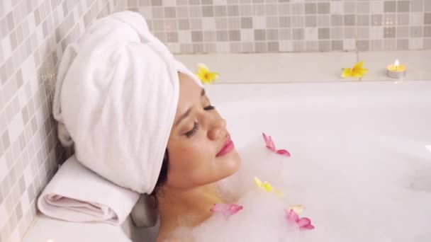 年轻的妇女在浴缸里休息 而她的头上戴着泡沫和鸡蛋花的毛巾 — 图库视频影像