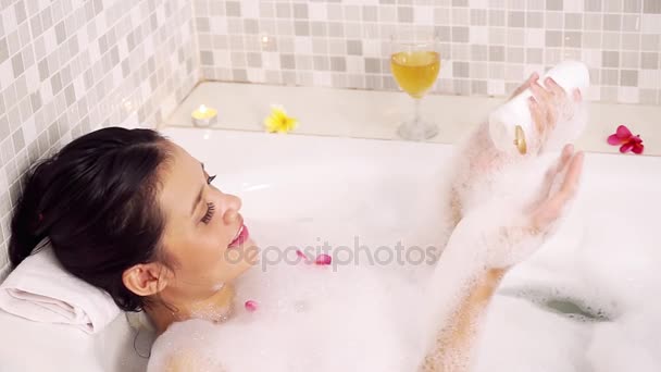 美丽的妇女使用液体肥皂或身体乳液在她的身体在浴缸与泡沫和鸡蛋花鲜花 — 图库视频影像