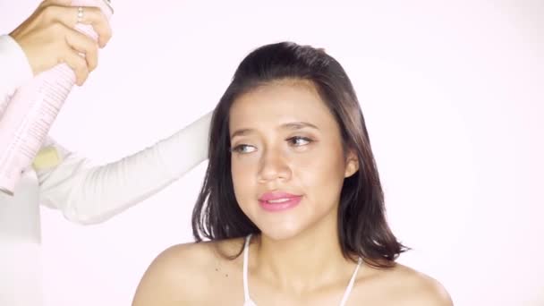 美丽的女性模型应用头发喷雾与她的发型师在工作室 孤立的白色背景 — 图库视频影像