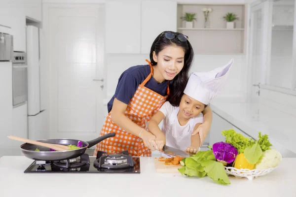 Мама учит свою дочь резать морковку — стоковое фото