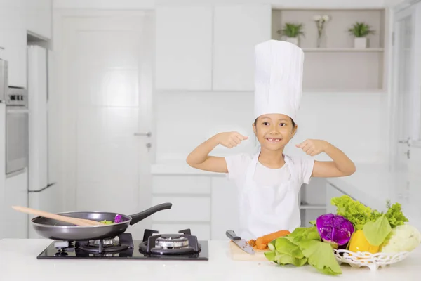 Маленькая девочка показывает свои бицепсы на кухне — стоковое фото