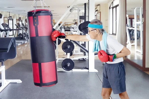 Elderly man punching a boxing bag — Stock Photo, Image