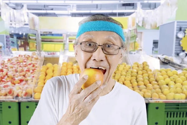 Homem idoso comendo uma maçã no supermercado — Fotografia de Stock
