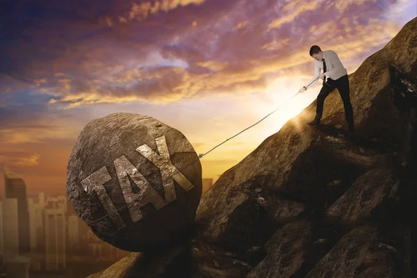 Caucasian businessman pulling tax word on the cliff — Stock Photo, Image