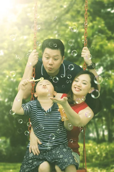 Feliz família soprando bolhas de sabão no parque infantil — Fotografia de Stock