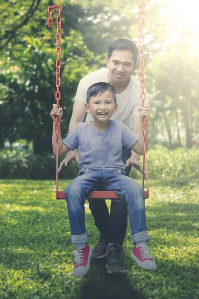 Gelukkig vader en zoon spelen met een schommel in park — Stockfoto