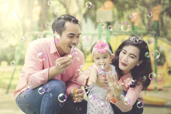 Pai e mãe brincando bolhas com a filha — Fotografia de Stock