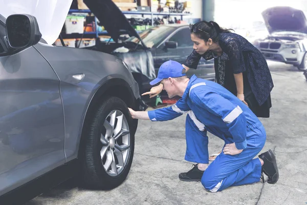 Kaukasiska mekaniker att hjälpa en kvinnlig kund kolla på ett däck — Stockfoto