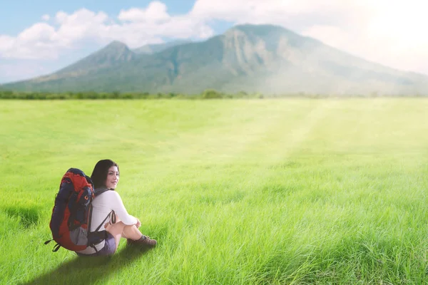 Asiatische Touristin sitzt mit Rucksack auf einem grünen Hügel — Stockfoto