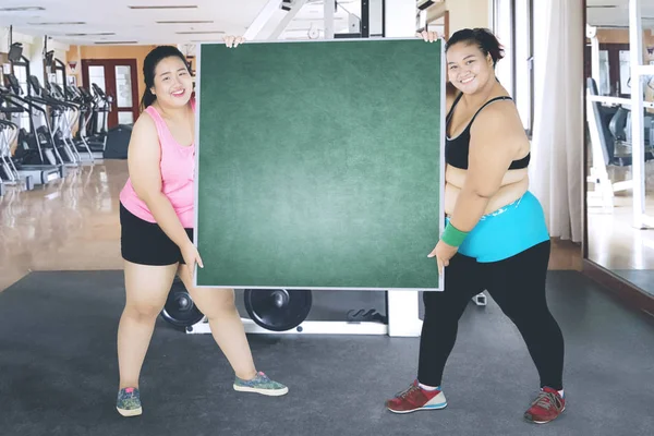 Two obese women lifting an empty board in gym