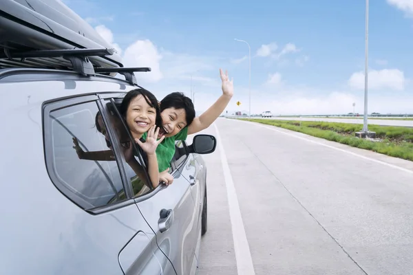 Happy sourozenci mává rukama, cestování autem proti modré obloze. — Stock fotografie