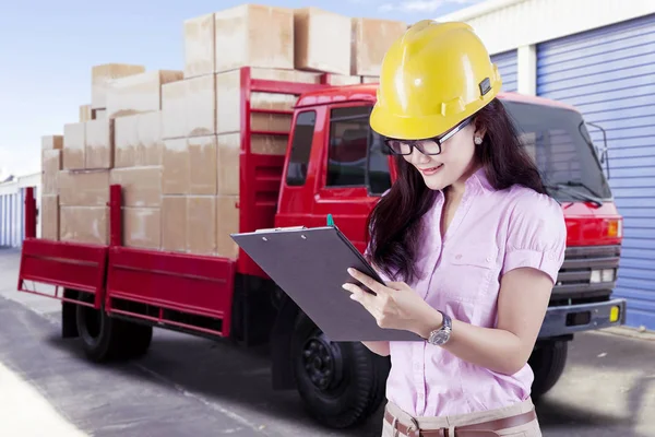Supervisor femenina con casco de seguridad mirando a través de la lista de verificación en frente de cajas de transporte de camiones — Foto de Stock