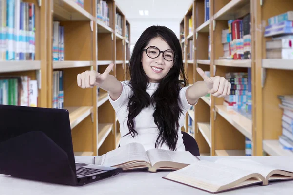 Kvinnlig student visar tummen i biblioteket — Stockfoto