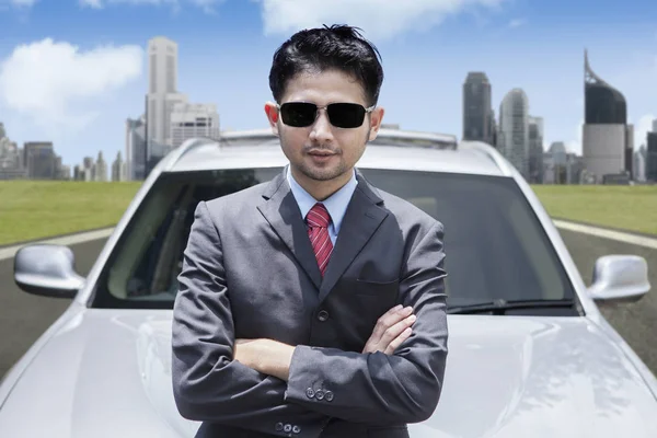 Homme d'affaires asiatique prospère portant des lunettes de soleil devant une voiture de luxe — Photo