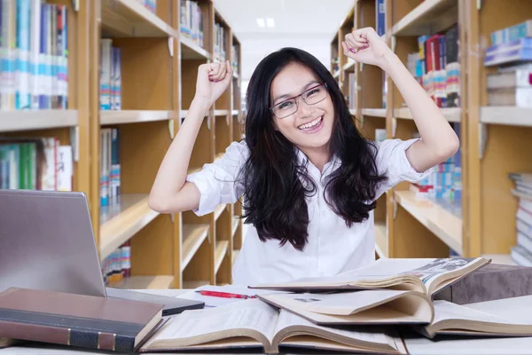 Estudante bonita levantando as mãos na biblioteca — Fotografia de Stock