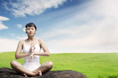 Asyalı kadın açık havada çayır mavi gökyüzü karşı kayaya üzerinde meditasyon