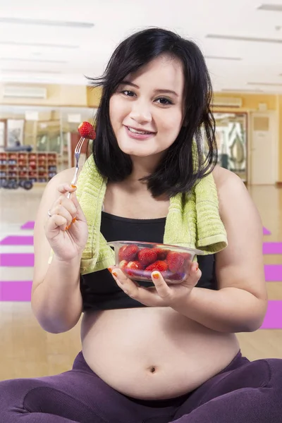 Красивая беременная женщина ест клубнику в спортзале — стоковое фото